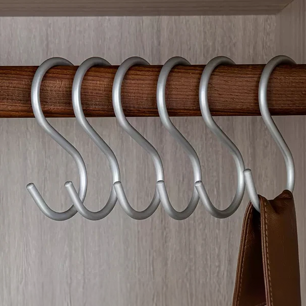 Five silver hooks on a wooden rod against a neutral wall.