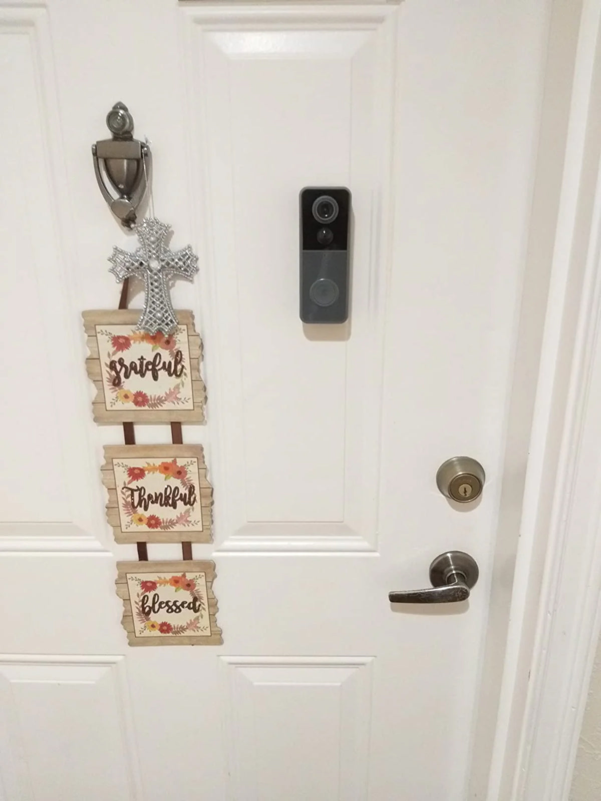 Decorative sign with 'Grateful', 'Thankful', and 'Blessed' on a door with a security camera.
