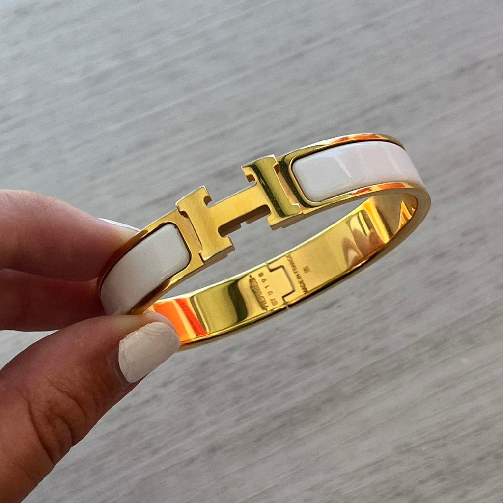 Gold and white bracelet held by a hand on a gray background