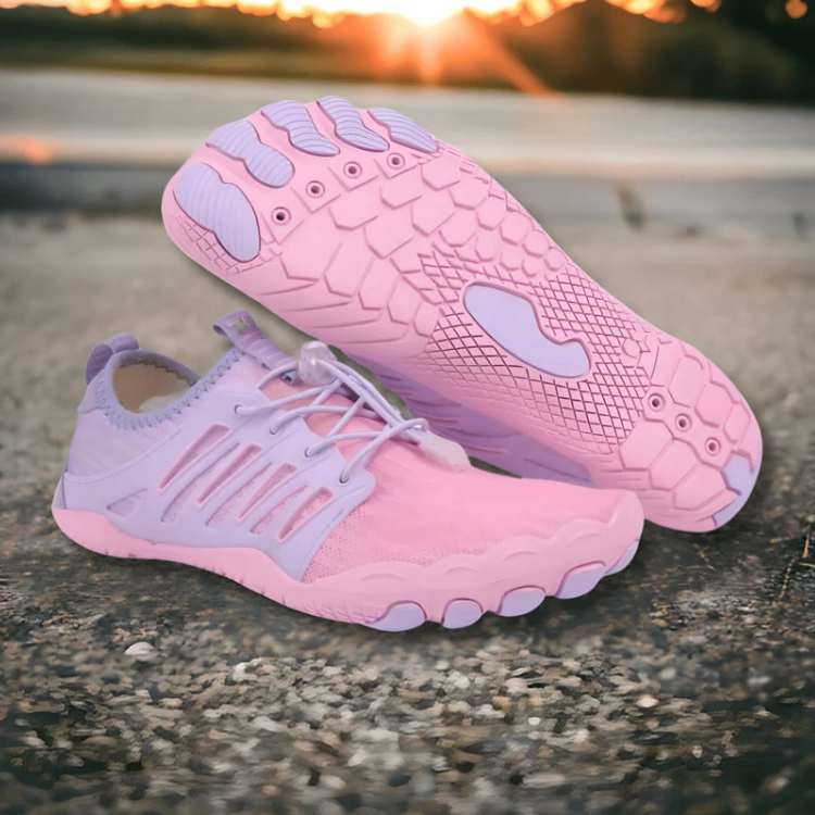Pink and purple running shoes on a concrete surface with a sunset background