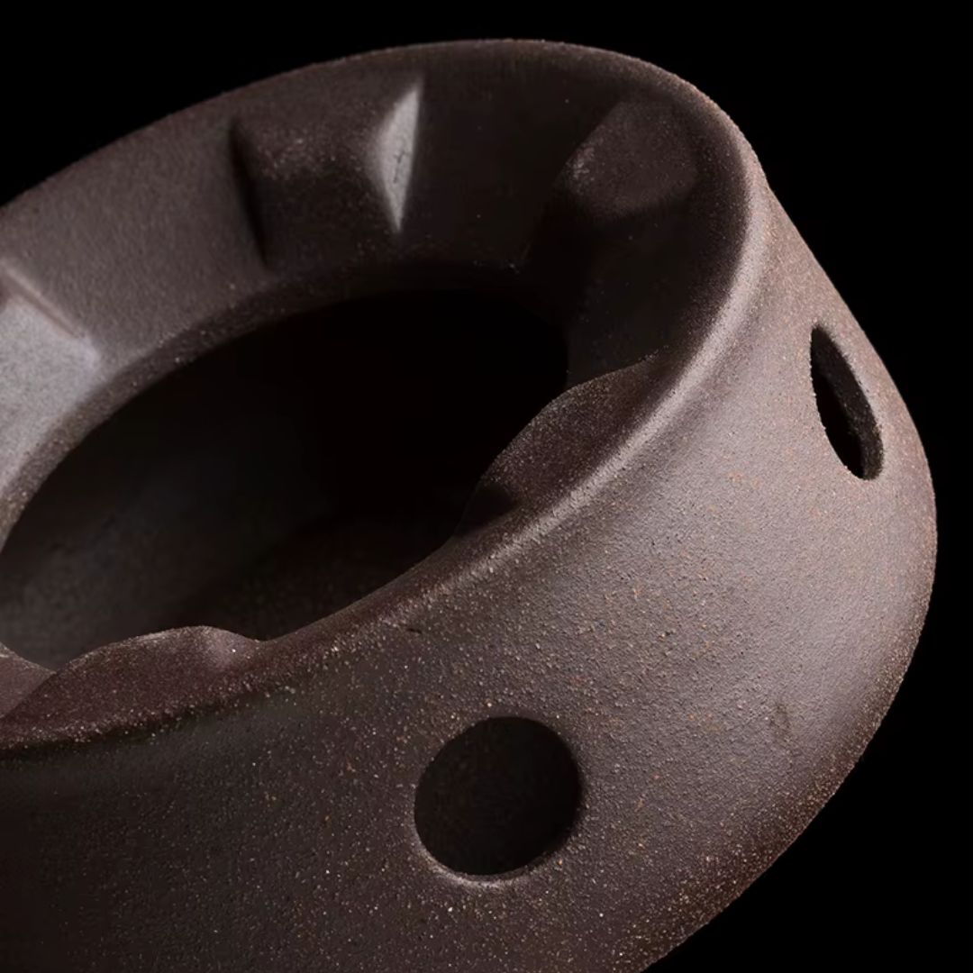Close-up of a dark brown ceramic pot with textured surface and circular holes on a black background