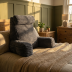 Gray textured armchair on a bed with wooden nightstands and lamp in a room.