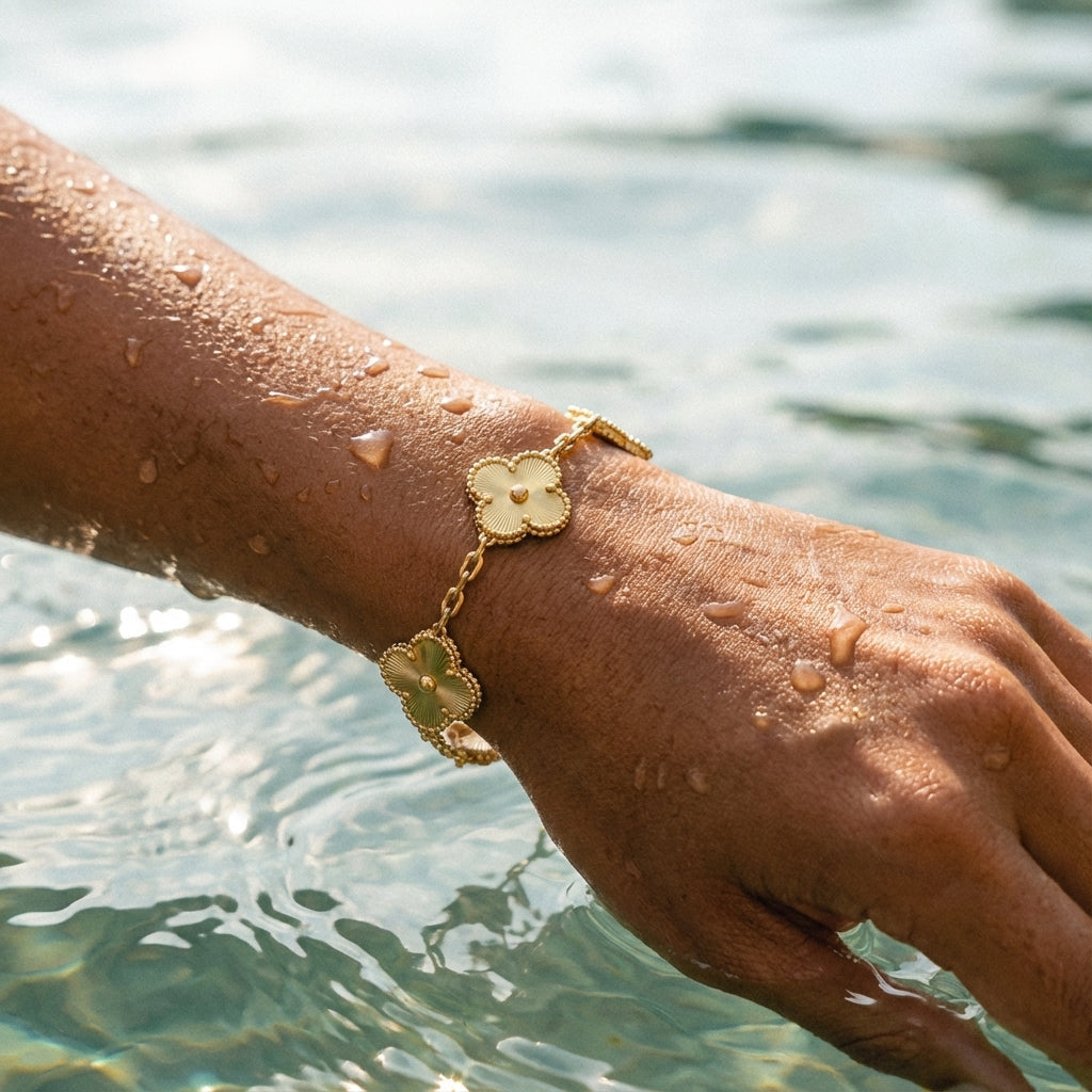 Hand wearing a gold bracelet with floral designs by a body of water.
