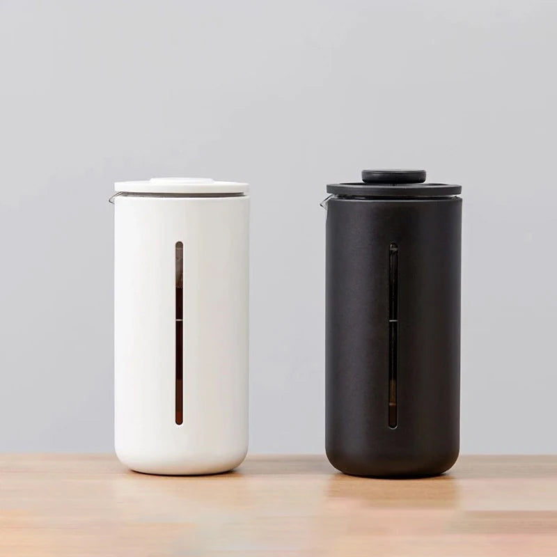 Two cylindrical containers, one white and one black, on a wooden surface with a light gray background.