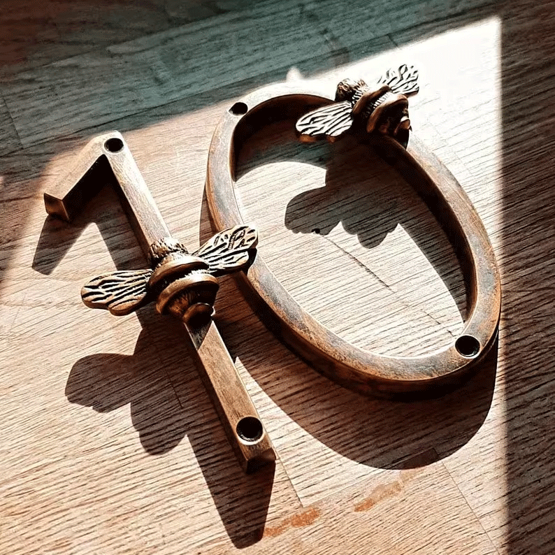 Decorative metal number '13' with bee designs on a wooden surface