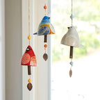 Colorful ceramic bird-shaped wind chimes hanging against a window.
