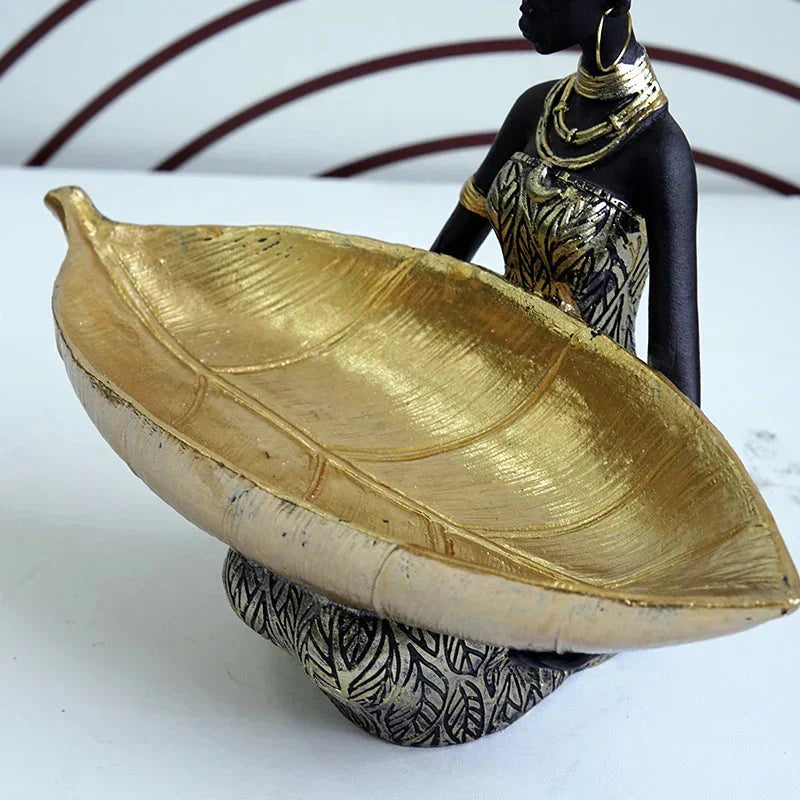 Decorative item with a gold leaf-shaped bowl and black and gold figure on a white background
