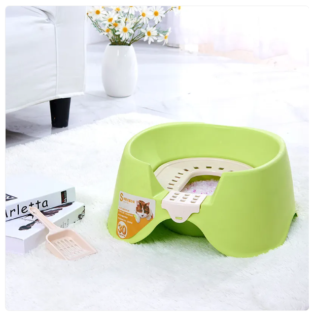 Green pet litter pan on a white carpet with a couch and flowers in the background