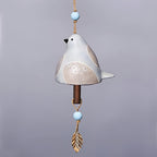 Decorative ceramic bird with beads and feather on a gray background