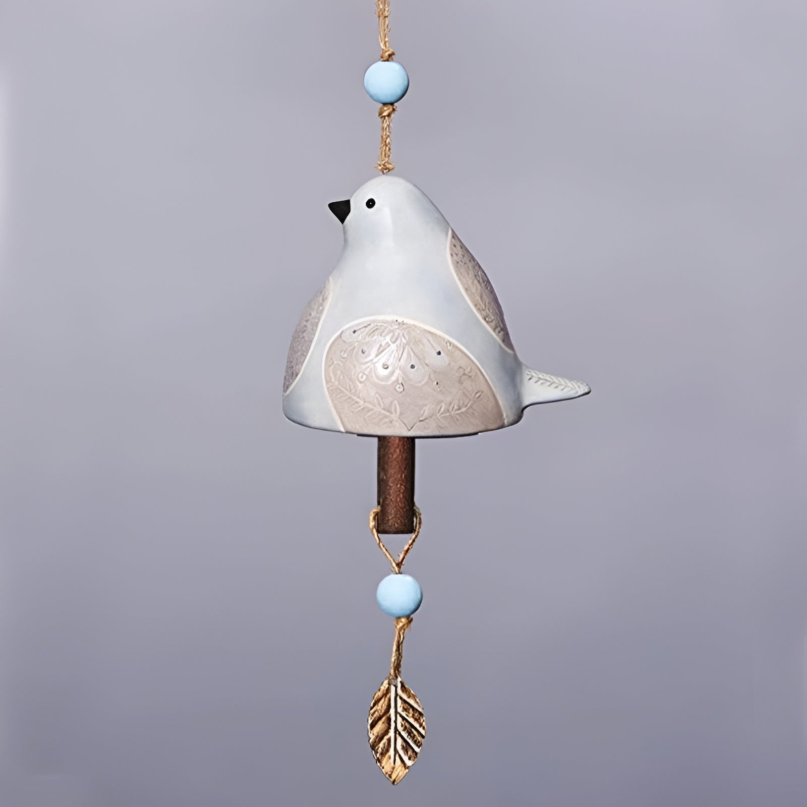 Decorative ceramic bird with beads and feather on a gray background