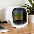 Small white fan on a desk with a laptop and plant in the background