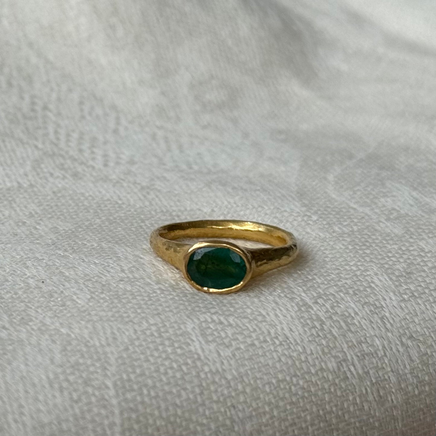 22ct Gold ring with a emerald gemstone on a light gray fabric background