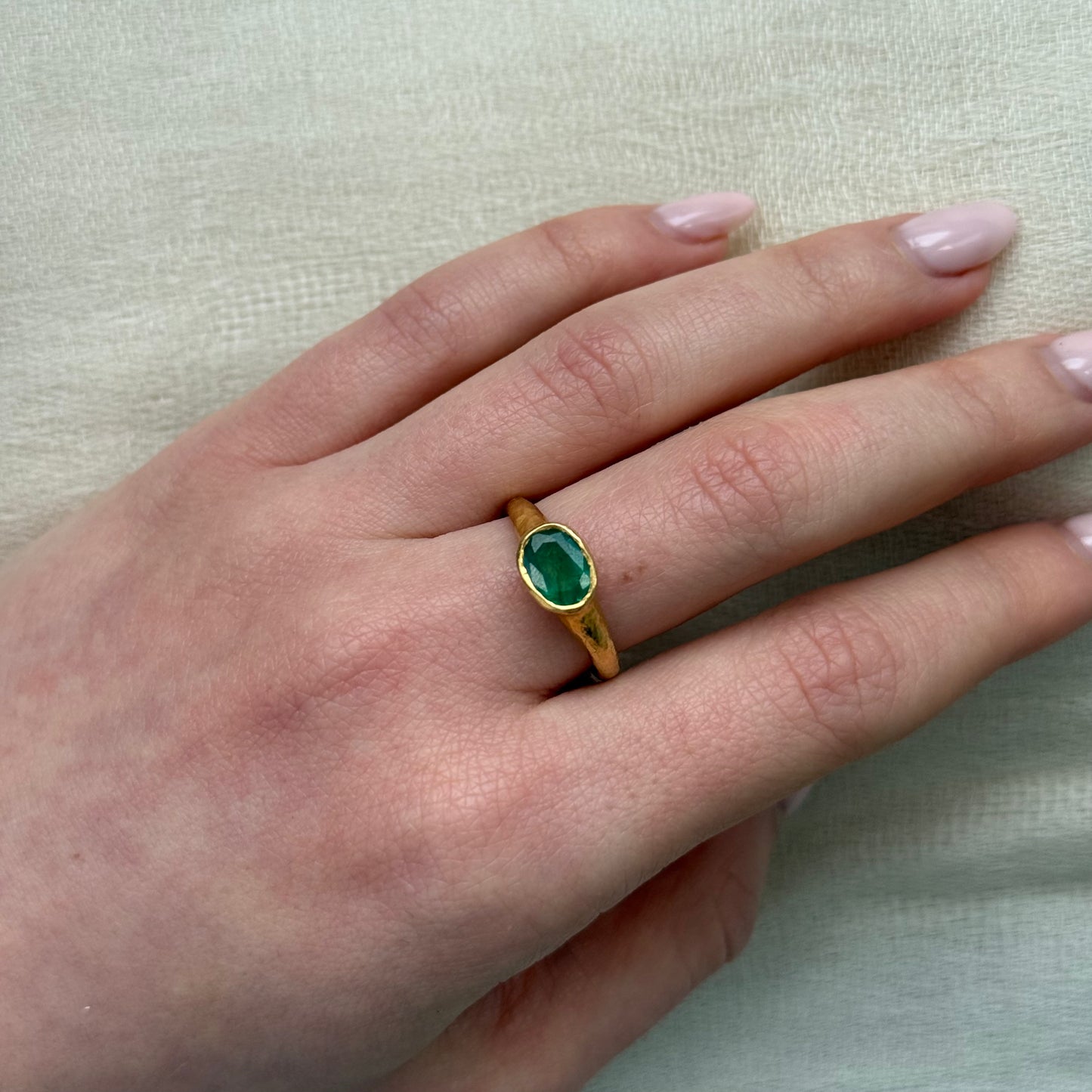 Hand wearing a 22ct gold ring with a green emerald on a light background