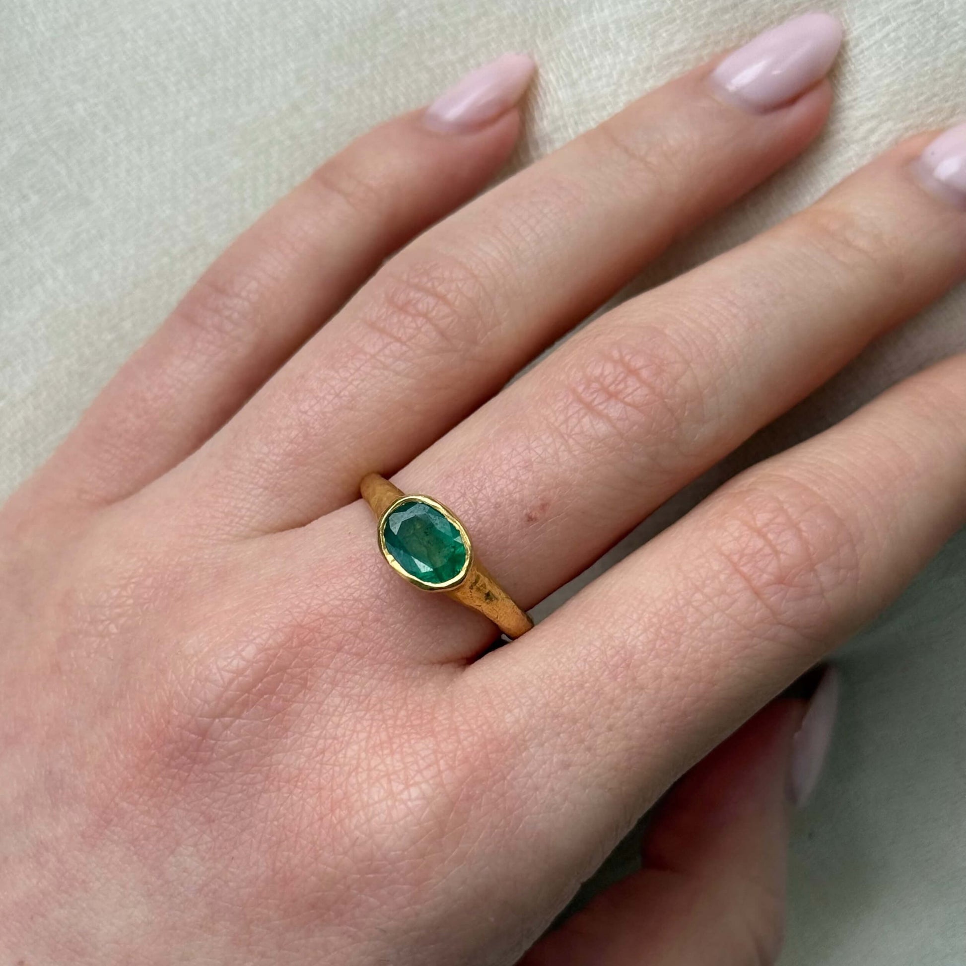 Gold ring with a green gemstone on a hand with light pink nail polish.
