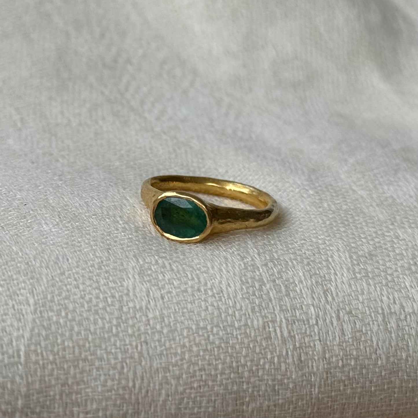 Gold ring with a green emerald on a light gray fabric background