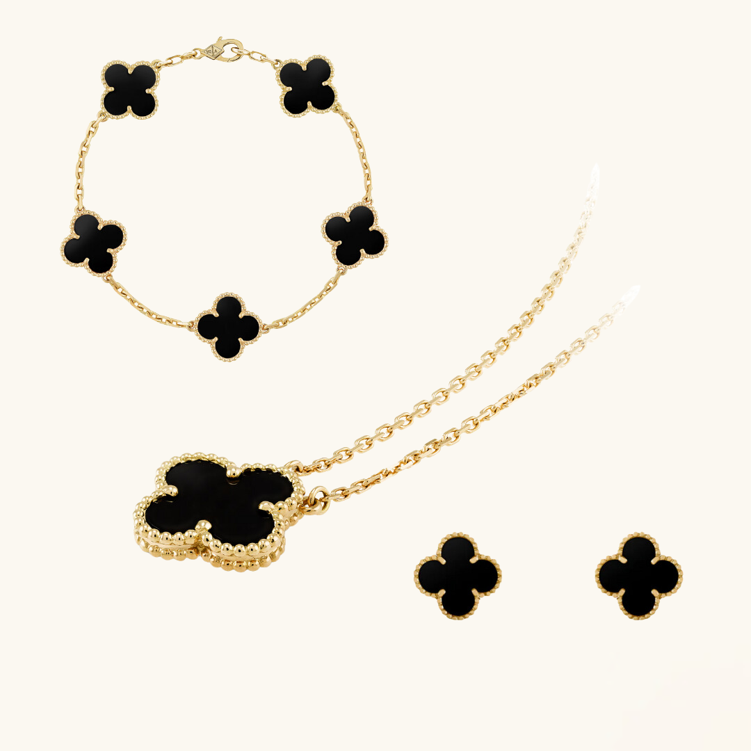 Gold jewelry set with black clover-shaped stones on a white background
