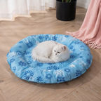 White cat lying on a blue pet bed with snowflake pattern on a wooden floor.
