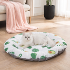 Cat lying on a round pet bed with avocado pattern in a living room.