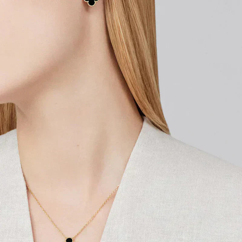 Person wearing a gold necklace with a small black pendant on a plain background