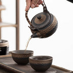 Ceramic teapot being poured into two cups on a tray with a blurred background