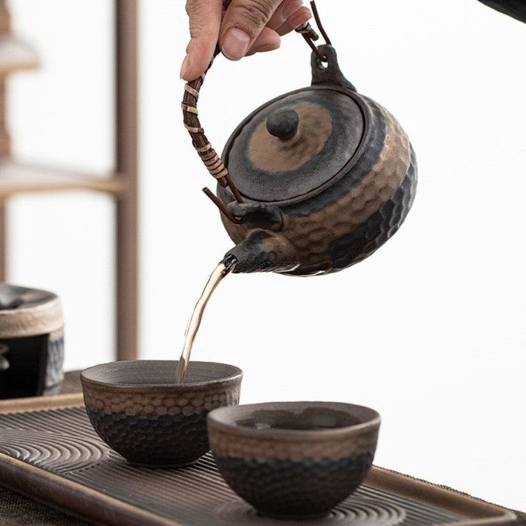 Ceramic teapot being poured into two cups on a tray with a blurred background