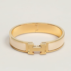 Gold bracelet with a brand logo on a light gray background
