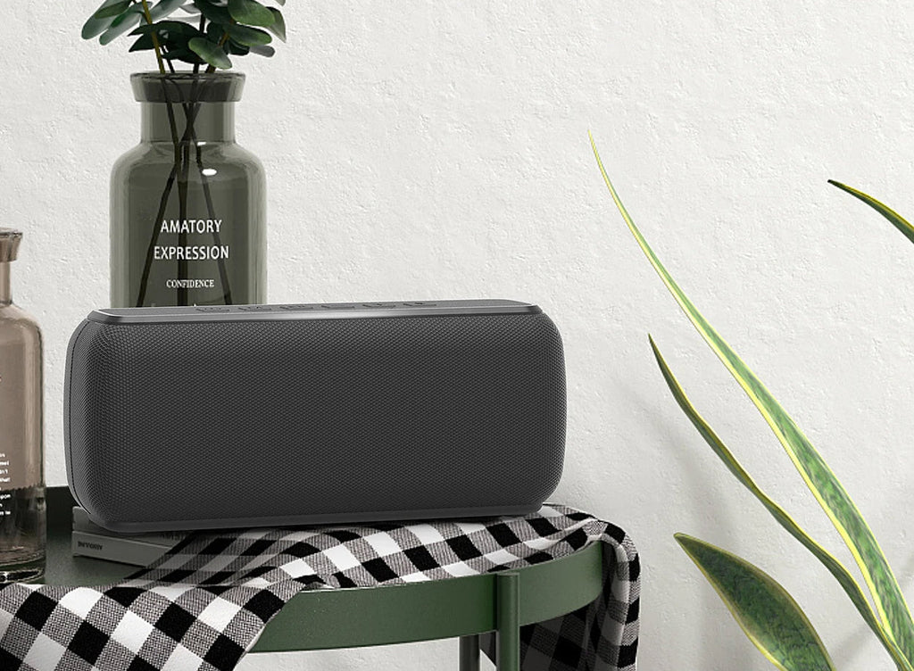 Black rectangular speaker on a checkered tablecloth with plants and a vase in the background