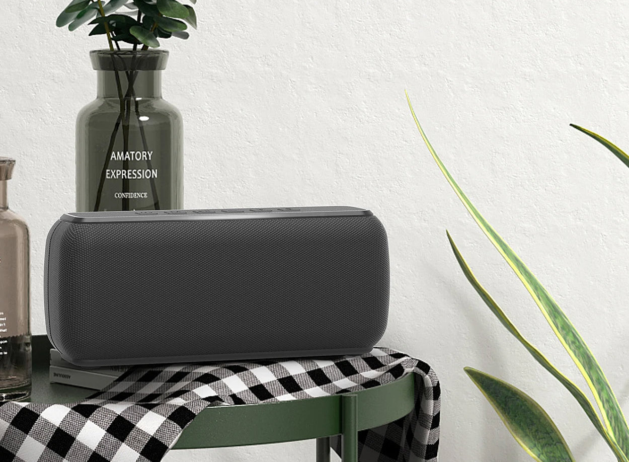 Black rectangular speaker on a checkered tablecloth with plants and a vase in the background
