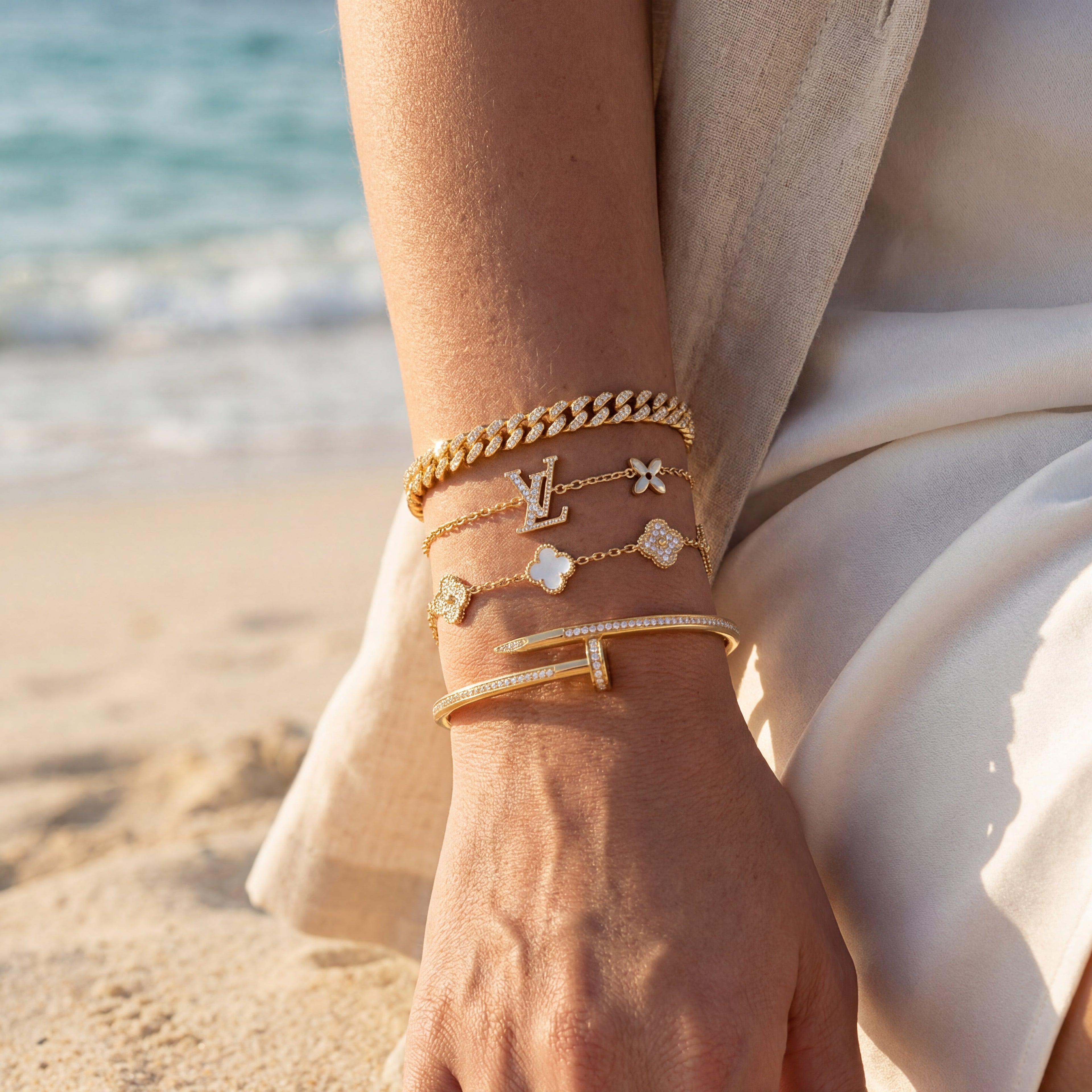 Close-up of a person's wrist wearing multiple gold bracelets with a beach background