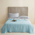 Bed with light blue comforter, gray pillows, and a beige headboard against a beige wall.