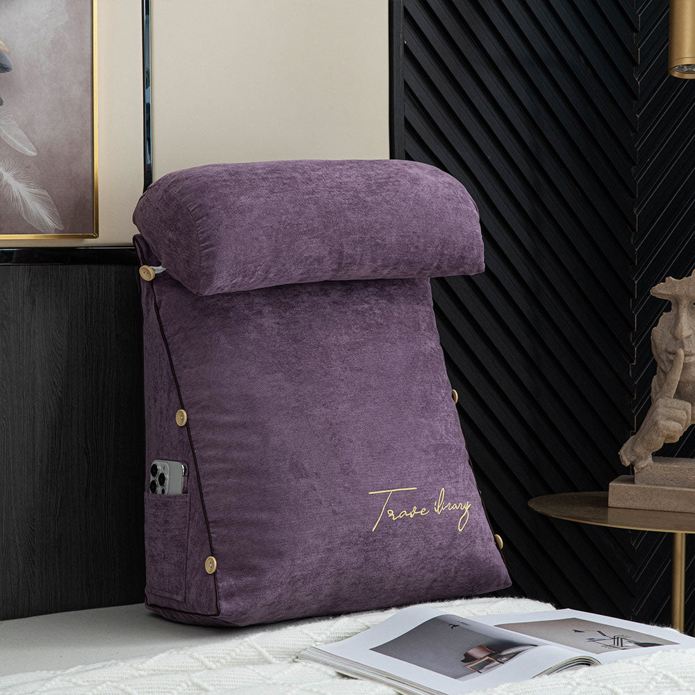Purple decorative pillow with 'Tasso Elba' branding on a surface with a black textured wall and framed picture in the background.