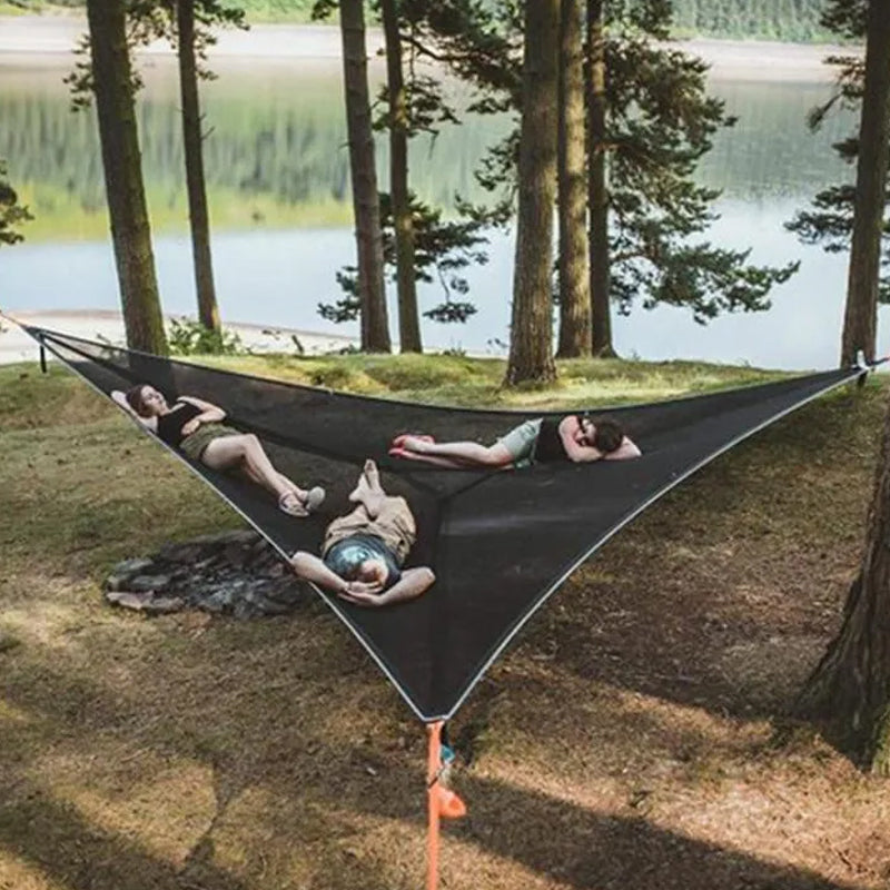 People relaxing in a large black hammock by a lake with trees in the background