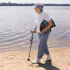 Person with a walking stick standing on a beach near water