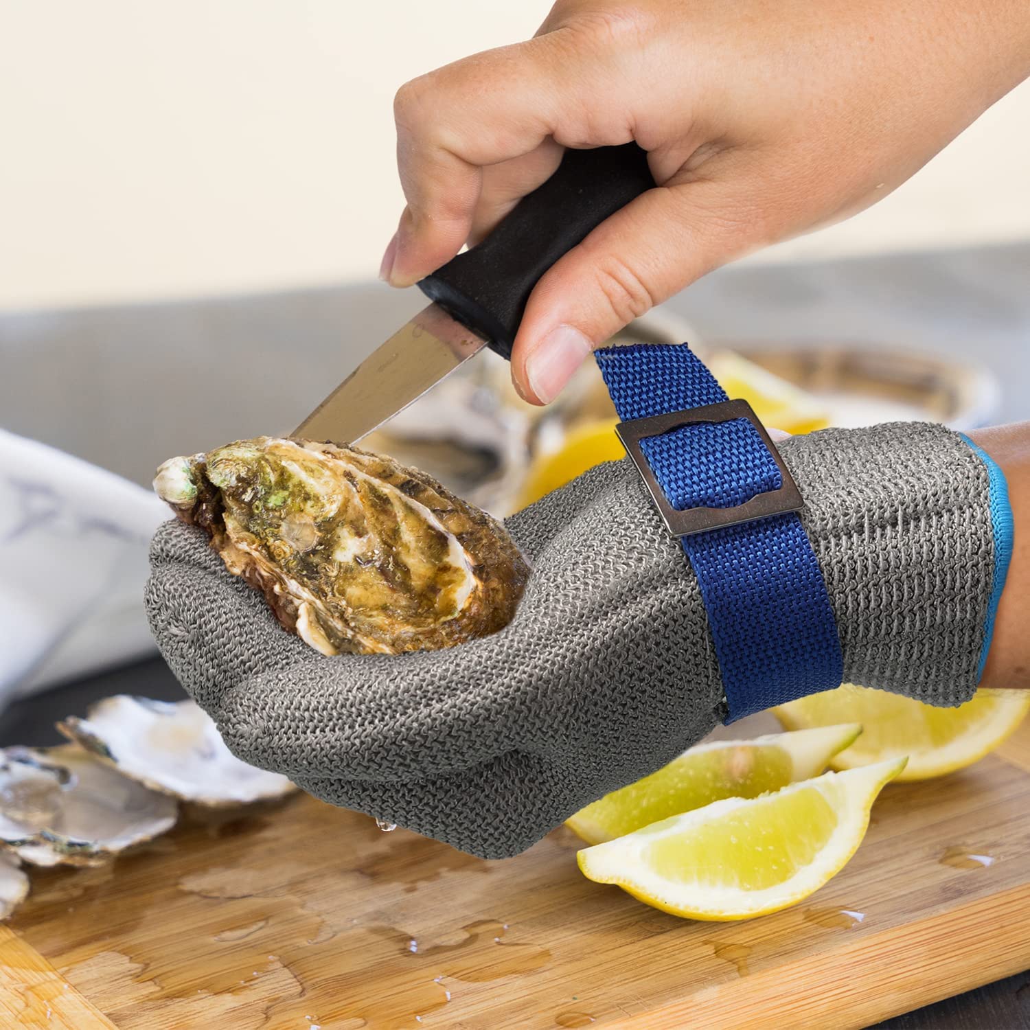 Person using an oyster shucking tool on a wooden cutting board with lemons