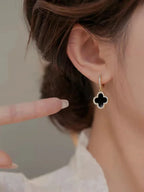 Close-up of a person wearing a black clover-shaped earring with gold accents.