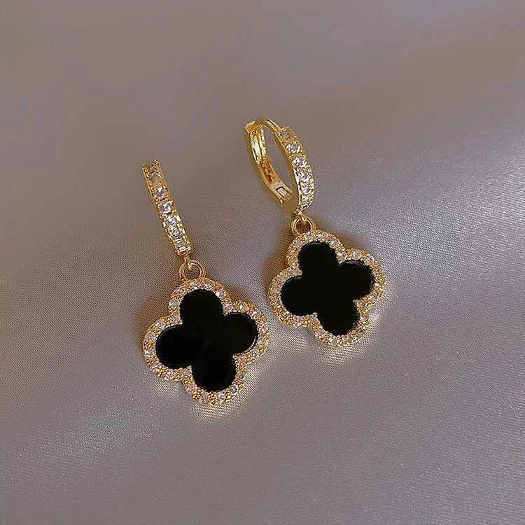 Gold earrings with black clover-shaped stones on a gray background