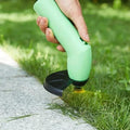 Hand using a green grass trimmer to cut grass along a concrete edge.