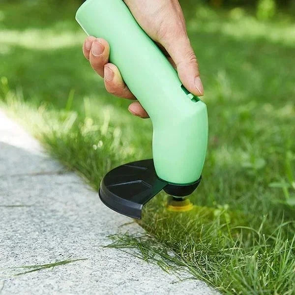 Hand using a green grass trimmer to cut grass along a concrete edge.
