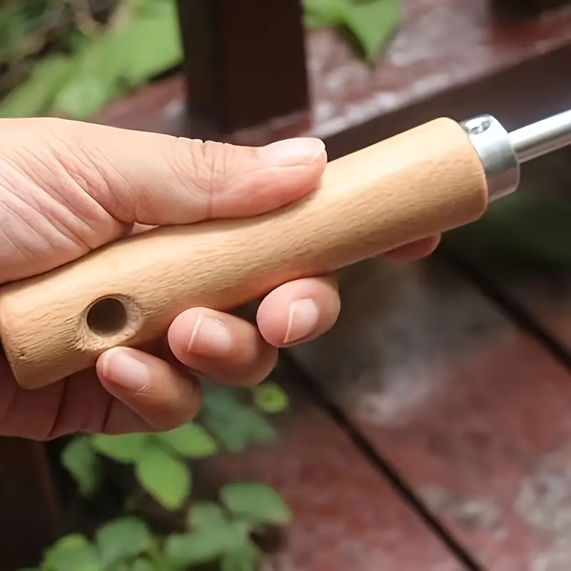 Hand holding a wooden tool with a metal end against a blurred natural background