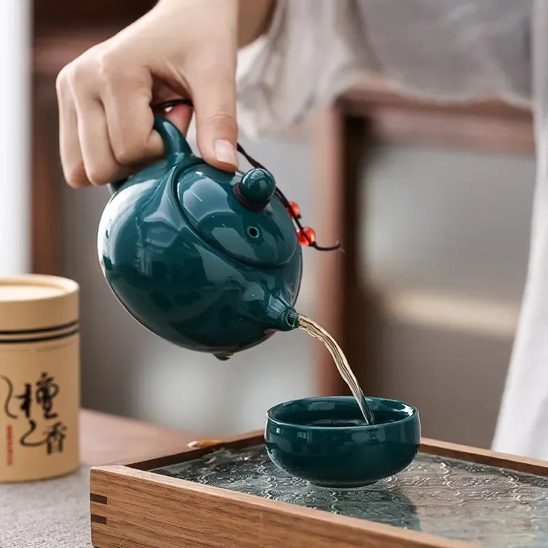 Tea being poured from a green teapot into a matching cup on a wooden tray.