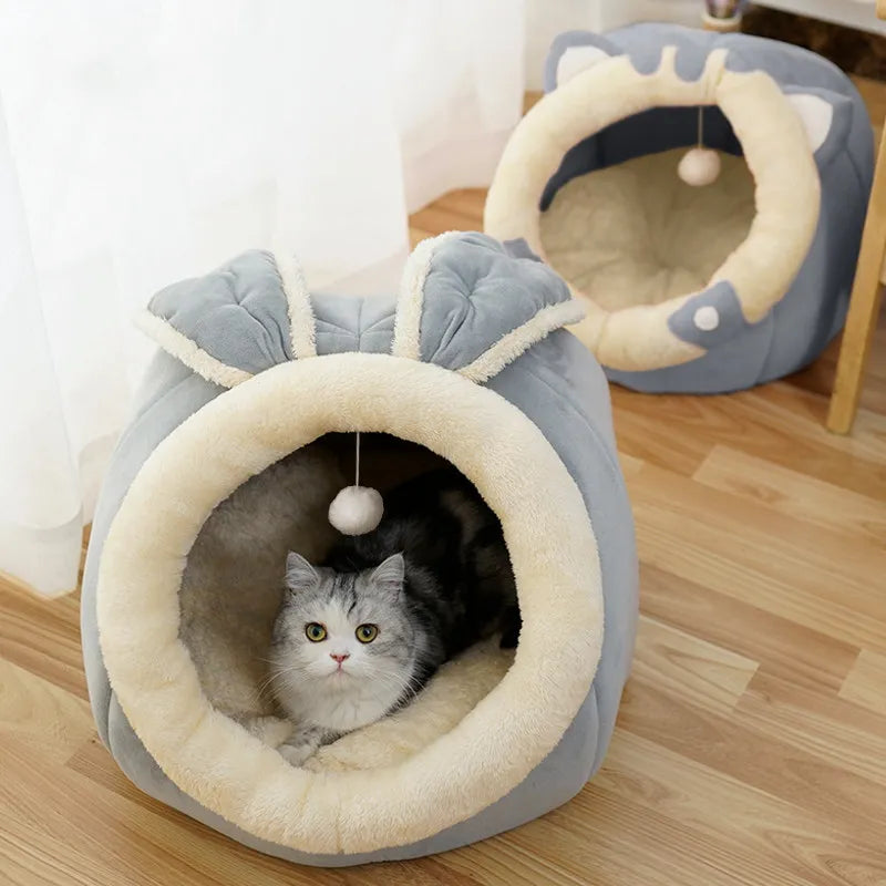Cat lying inside a gray pet bed with bunny ears on a wooden floor.