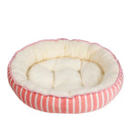 Round pet bed with pink and white striped exterior and cream interior on a white background