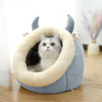 Cat inside a gray pet bed with animal ears and a tail on a wooden floor.
