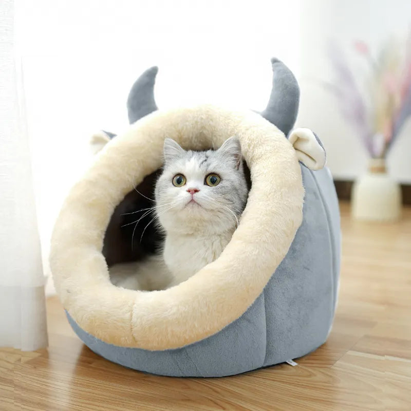 Cat inside a gray pet bed with animal ears and a tail on a wooden floor.