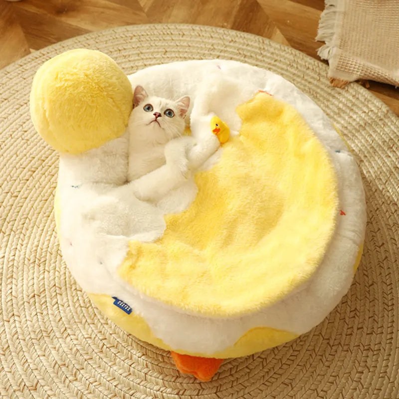 Cat lying on a yellow and white pet bed with plush toys on a wooden floor.