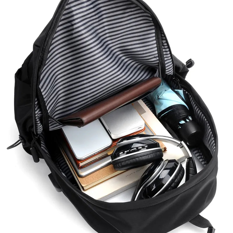 Black backpack with striped lining containing electronic devices and books on a white background