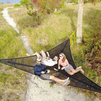 People relaxing on a large black hammock in a natural setting