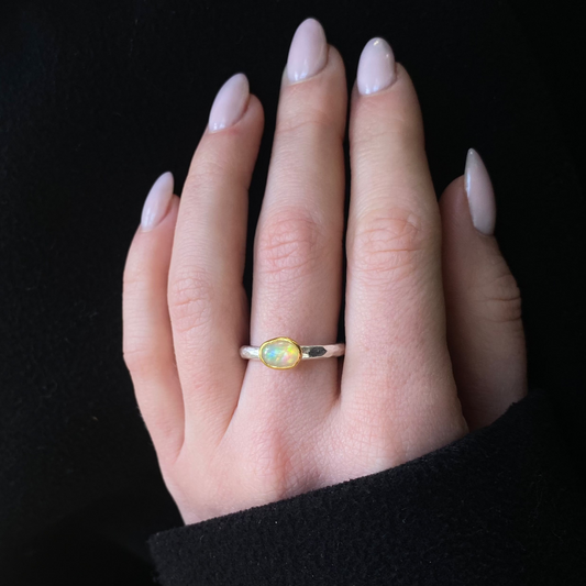 Hand wearing a ring with an opal stone, 22ct gold, silver against a black background