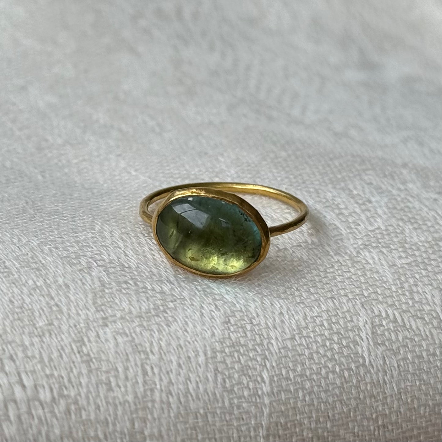 22ctGold ring with a green tourmaline gemstone on a textured beige surface