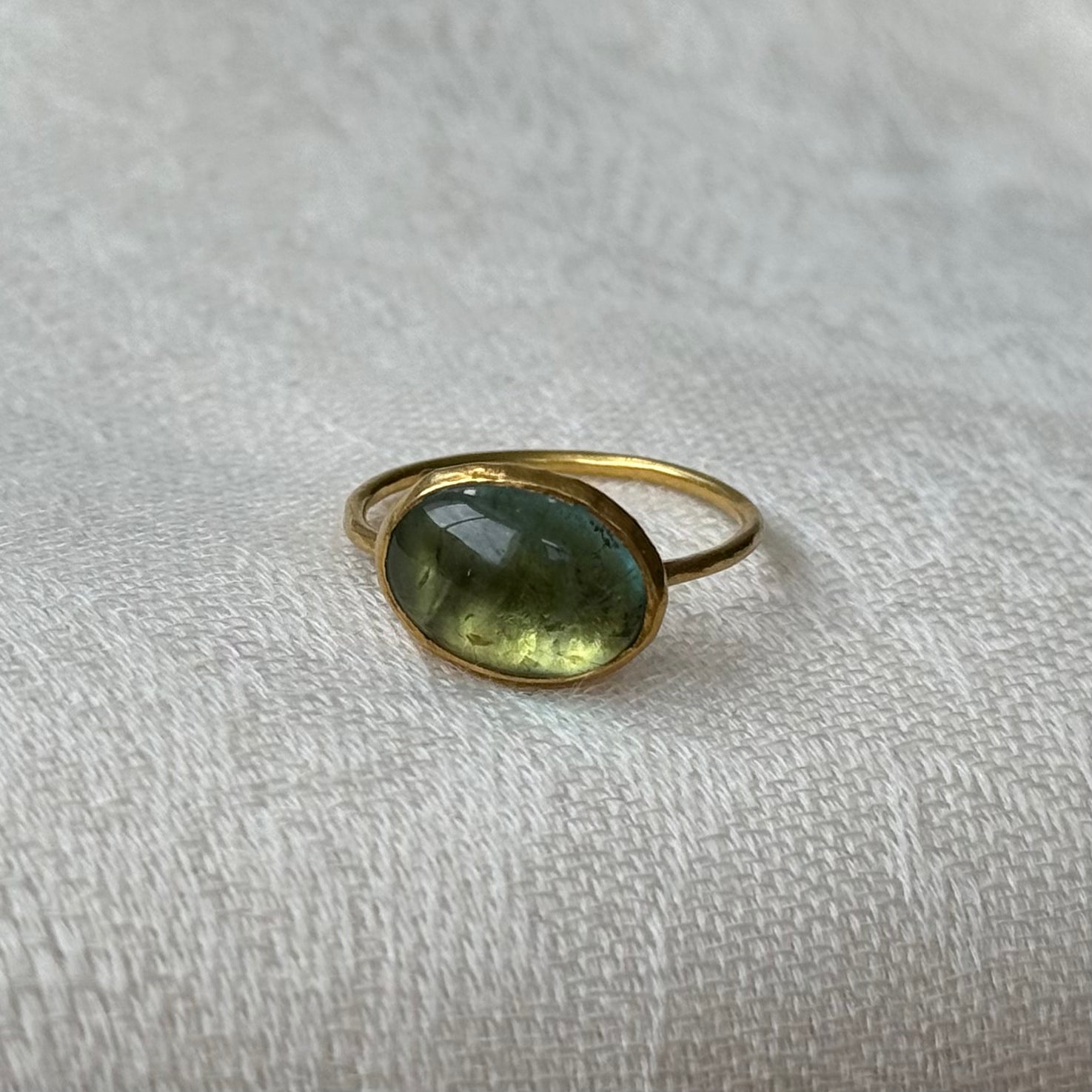 22ctGold ring with a green tourmaline gemstone on a textured beige surface
